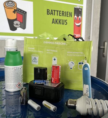 AWS Wertstoff-Sammeltasche mit unterschiedlichen Wertstoffen zur Verbildlichung davor: Spraydosen, Batterien, Akkus, Leuchtmittel, elektrische Zahnbürste