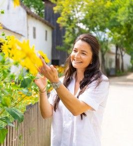 Frau steht an Gartenzaun und betrachtet gelbe Blumen