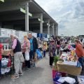 Flohmarkt am Sammelzentrum: Verkaufsstände und Personen, die einkaufen und verkaufen.