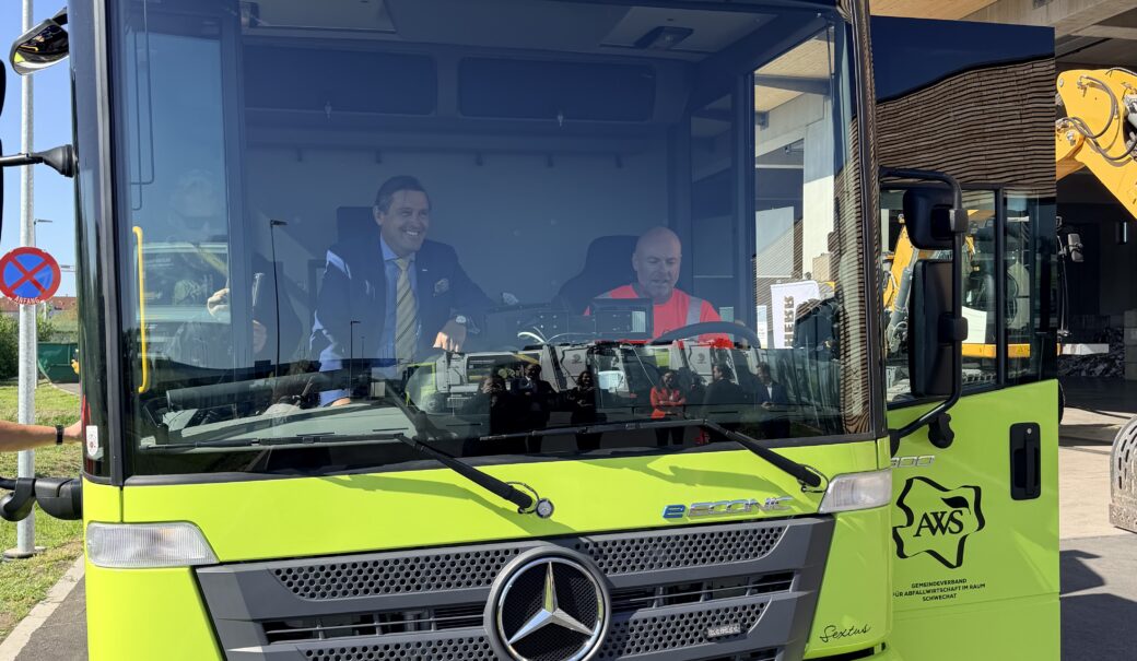 Grünes E-Müllabfuhr Auto des AWS von vorne. Bundesminister Hanke am Beifahrersitz, ein AWS Fahrer am Fahrersitz